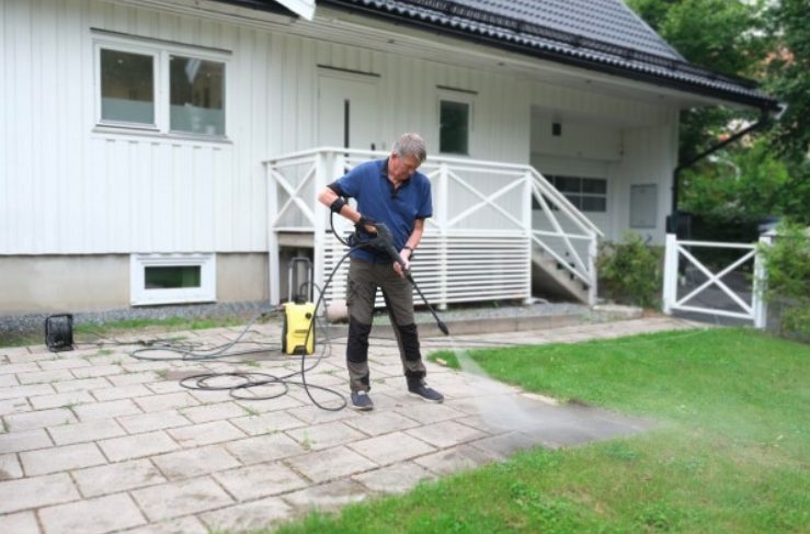 Ein Mann mit Carbonhand reinigt die Terrasse mit dem Hochdruckreiniger